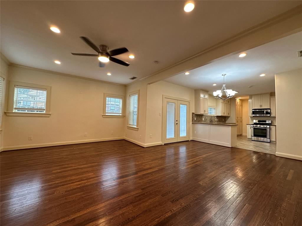 a view of an empty room with wooden floor and a kitchen