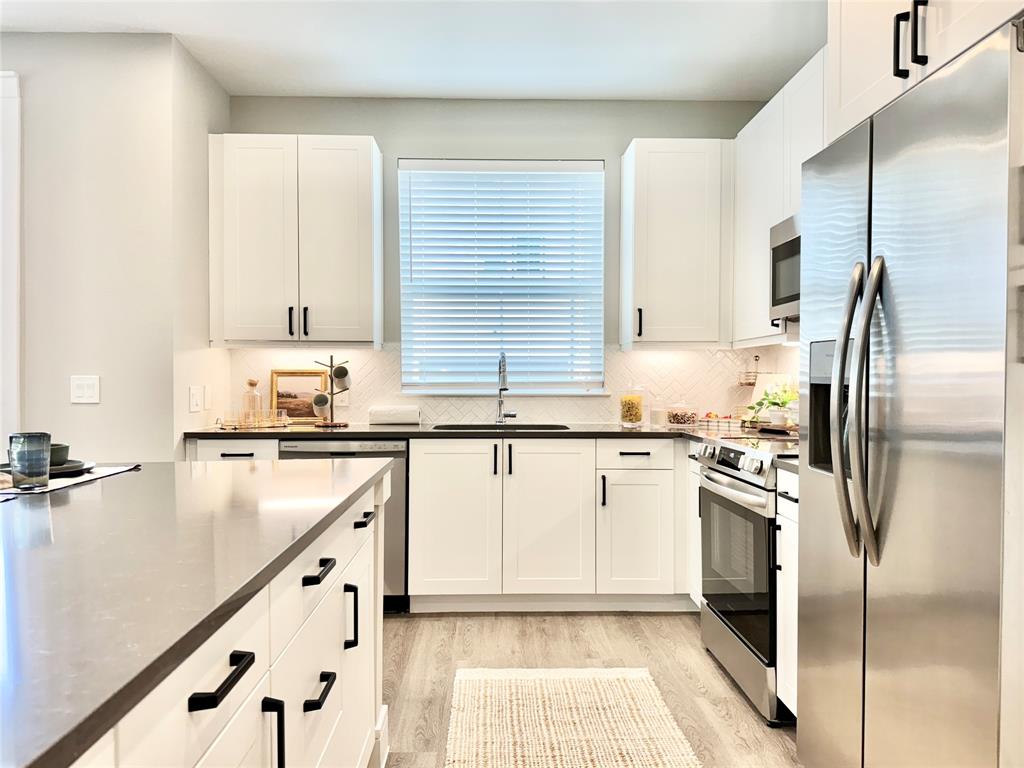 a kitchen with granite countertop a refrigerator a sink and white cabinets