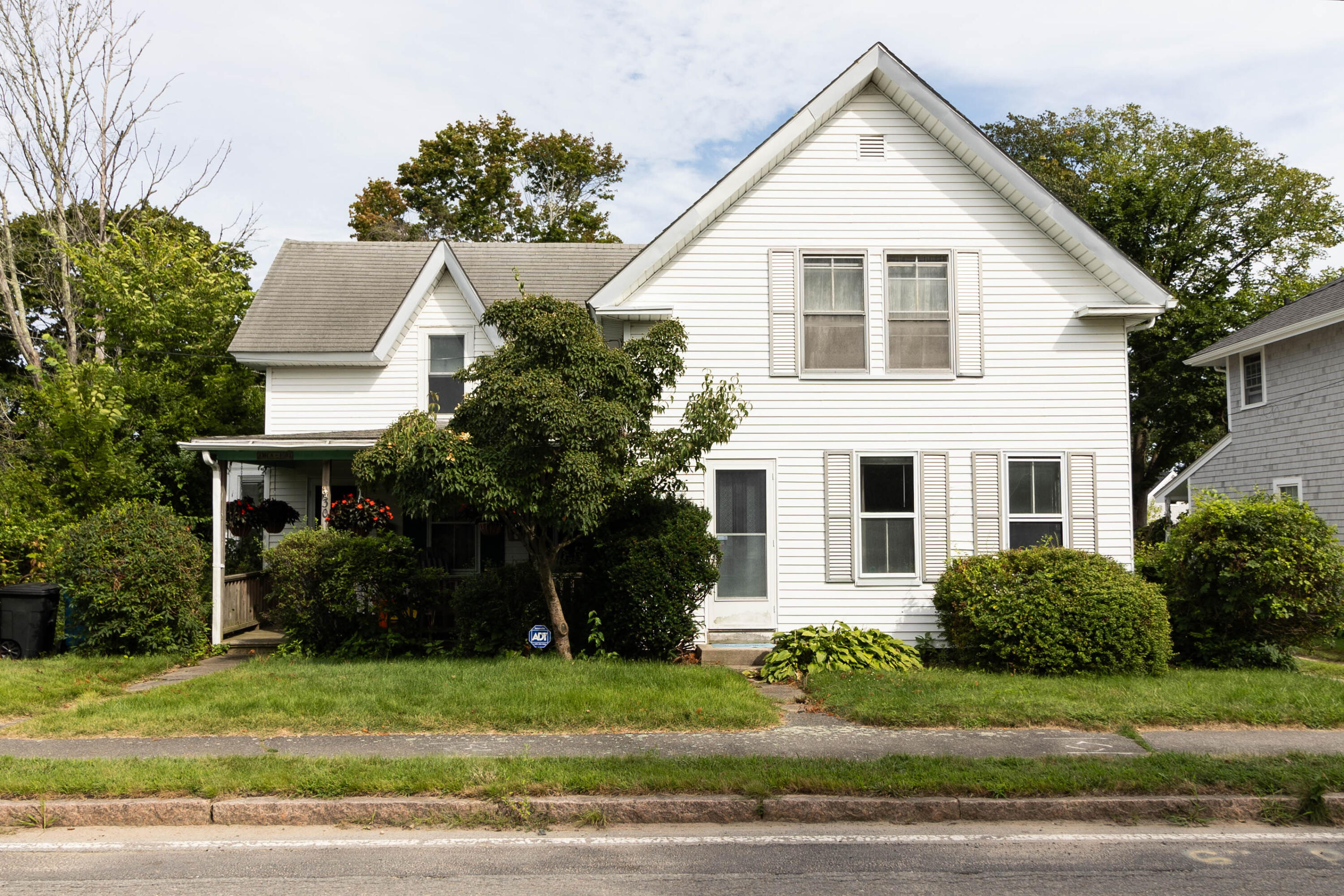 a view of a white house next to a yard with big trees