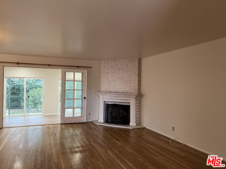 an empty room with wooden floor fireplace and windows