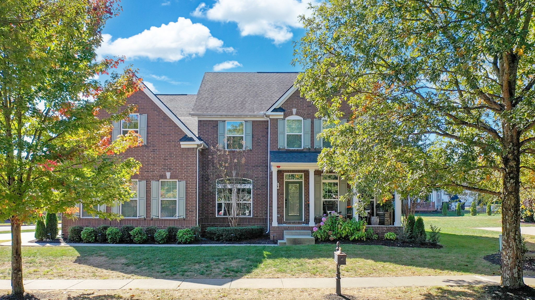 a view of a brick house next to a yard with big trees