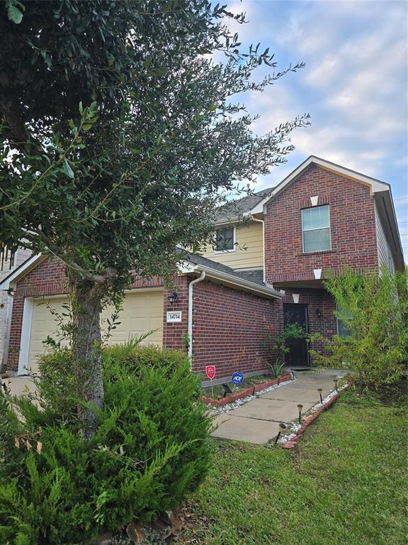 This is a two-story brick home featuring a prominent gable, an attached two-car garage, and a landscaped walkway leading to the front entrance, nestled among mature landscaping.