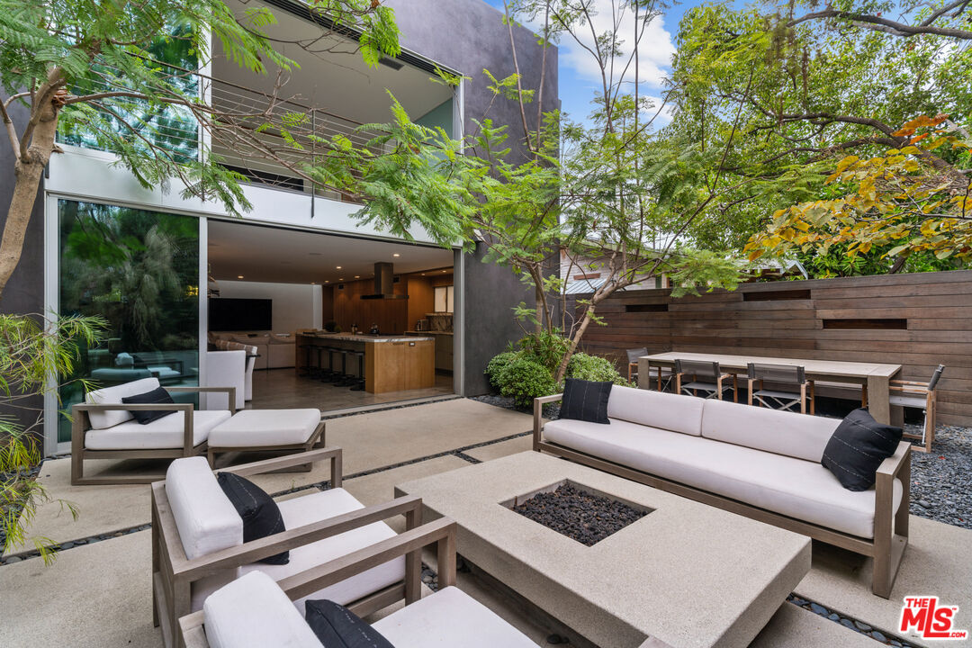 a view of a patio with couches table and chairs with potted plants and large trees