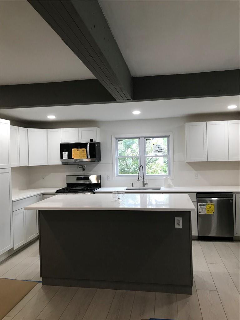 Kitchen with dishwasher, beam ceiling, sink, stove, and white cabinets