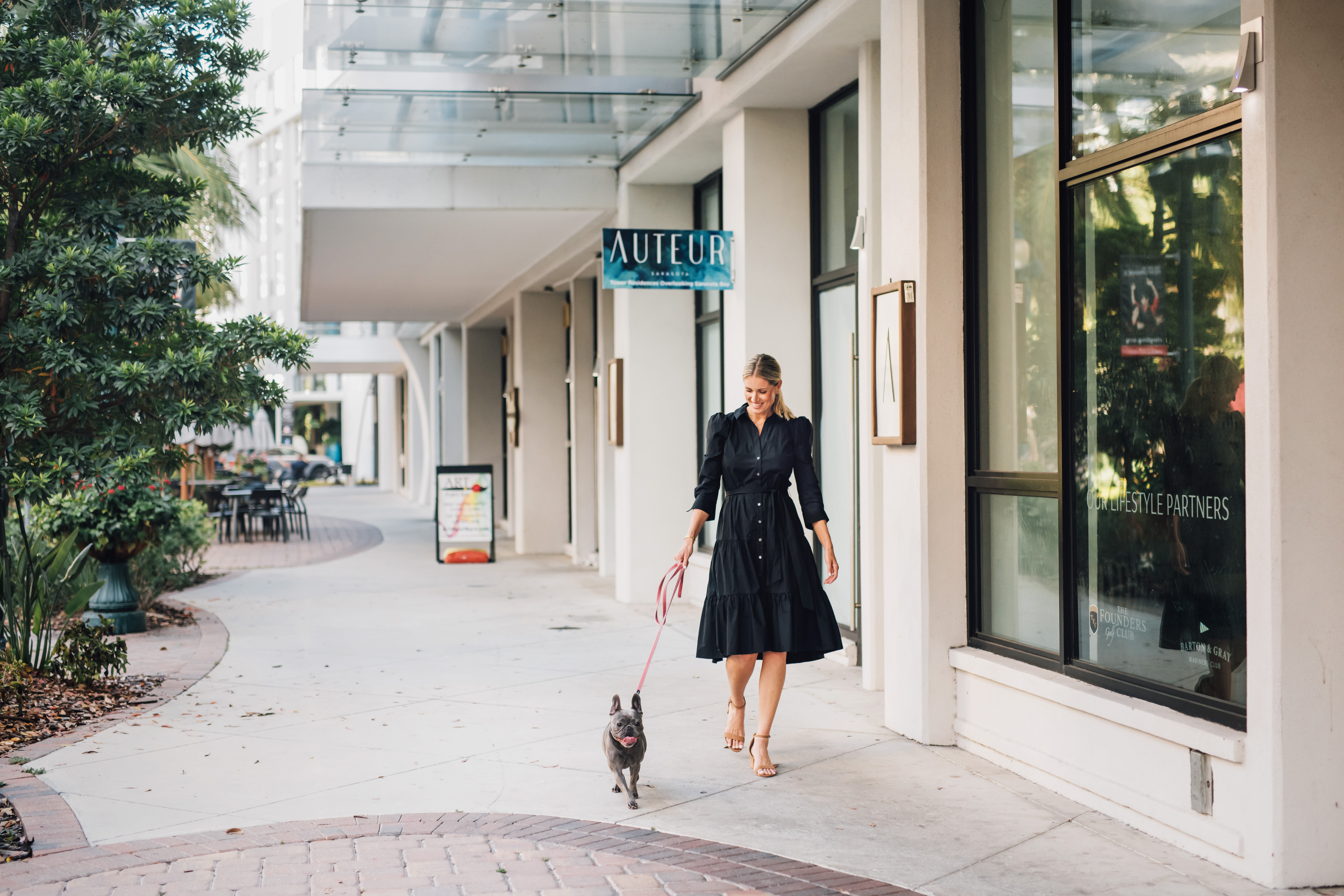 The caption for the given image is A woman walking down a sidewalk with a dog.