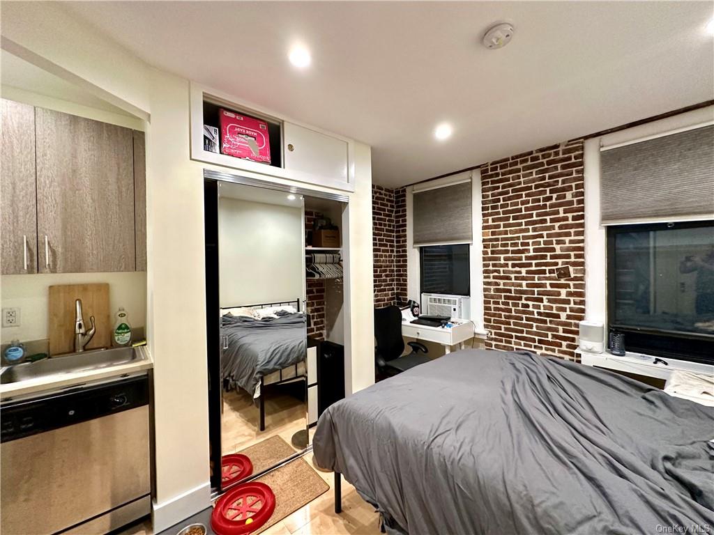 Bedroom with a closet, cooling unit, sink, light hardwood / wood-style floors, and brick wall