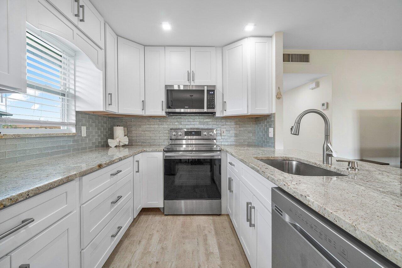 a kitchen with granite countertop a sink stainless steel appliances and white cabinets