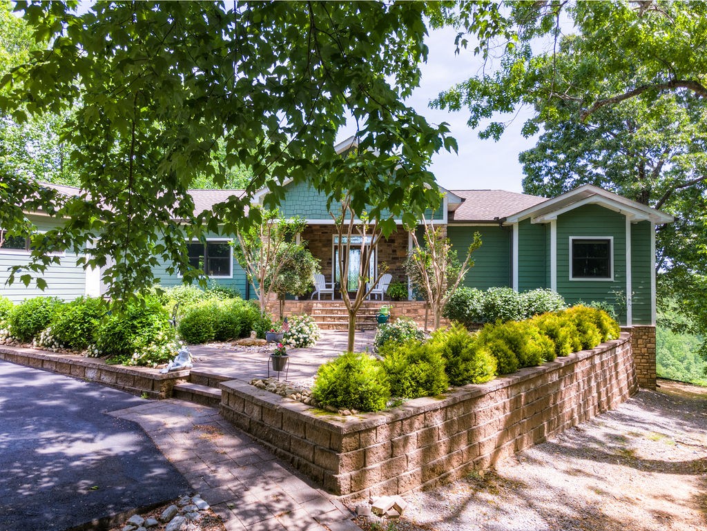 a front view of a house with lots of potted plants and large trees