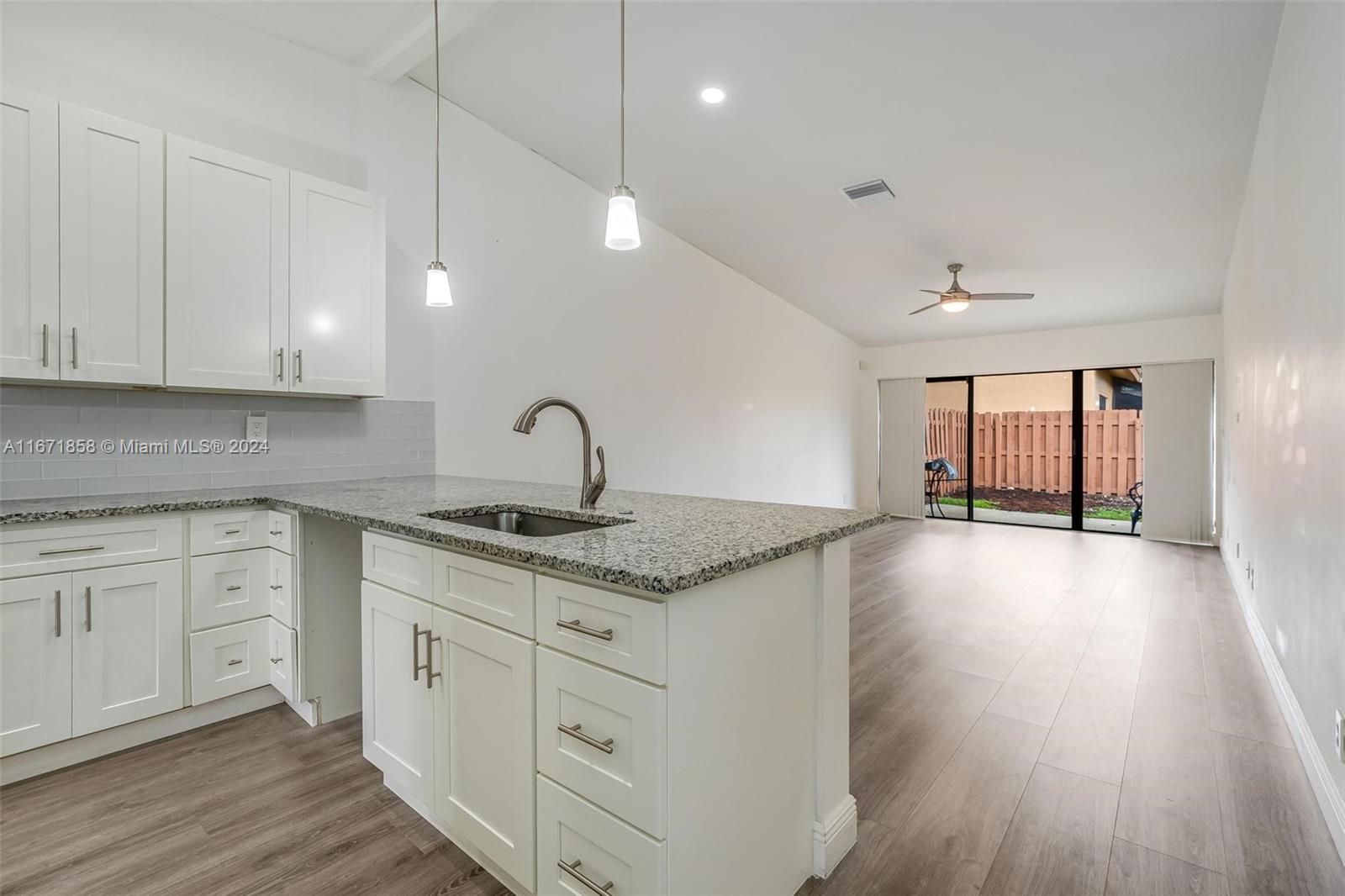 a kitchen with granite countertop a stove a sink and white cabinets with wooden floor next to windows