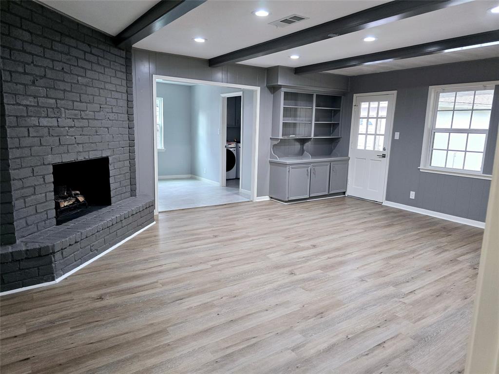 This spacious family room features a modern gray brick fireplace, vinyl plank flooring, and built-in shelving. The room is bright with recessed lighting, and it opens to an adjacent breakfast room through a wide doorway.