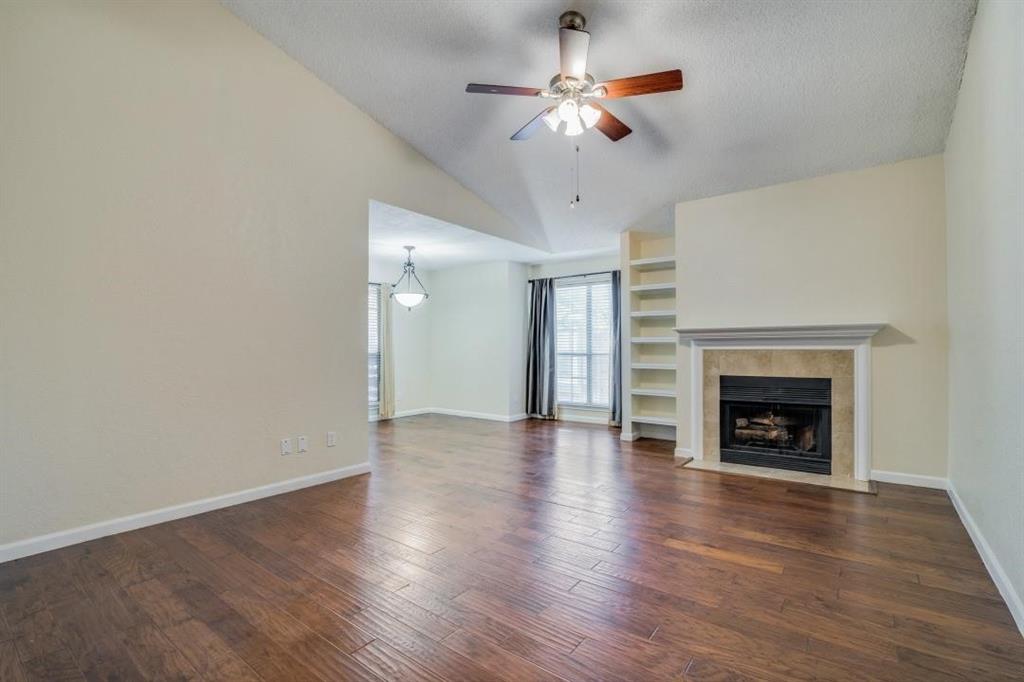 an empty room with wooden floor fireplace and chandelier fan