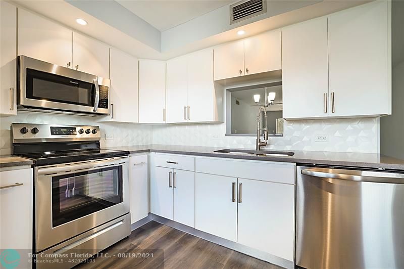 a kitchen with stainless steel appliances granite countertop white cabinets a sink and a stove