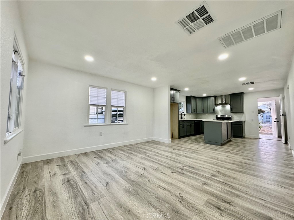 an empty room with wooden floor kitchen view and a window