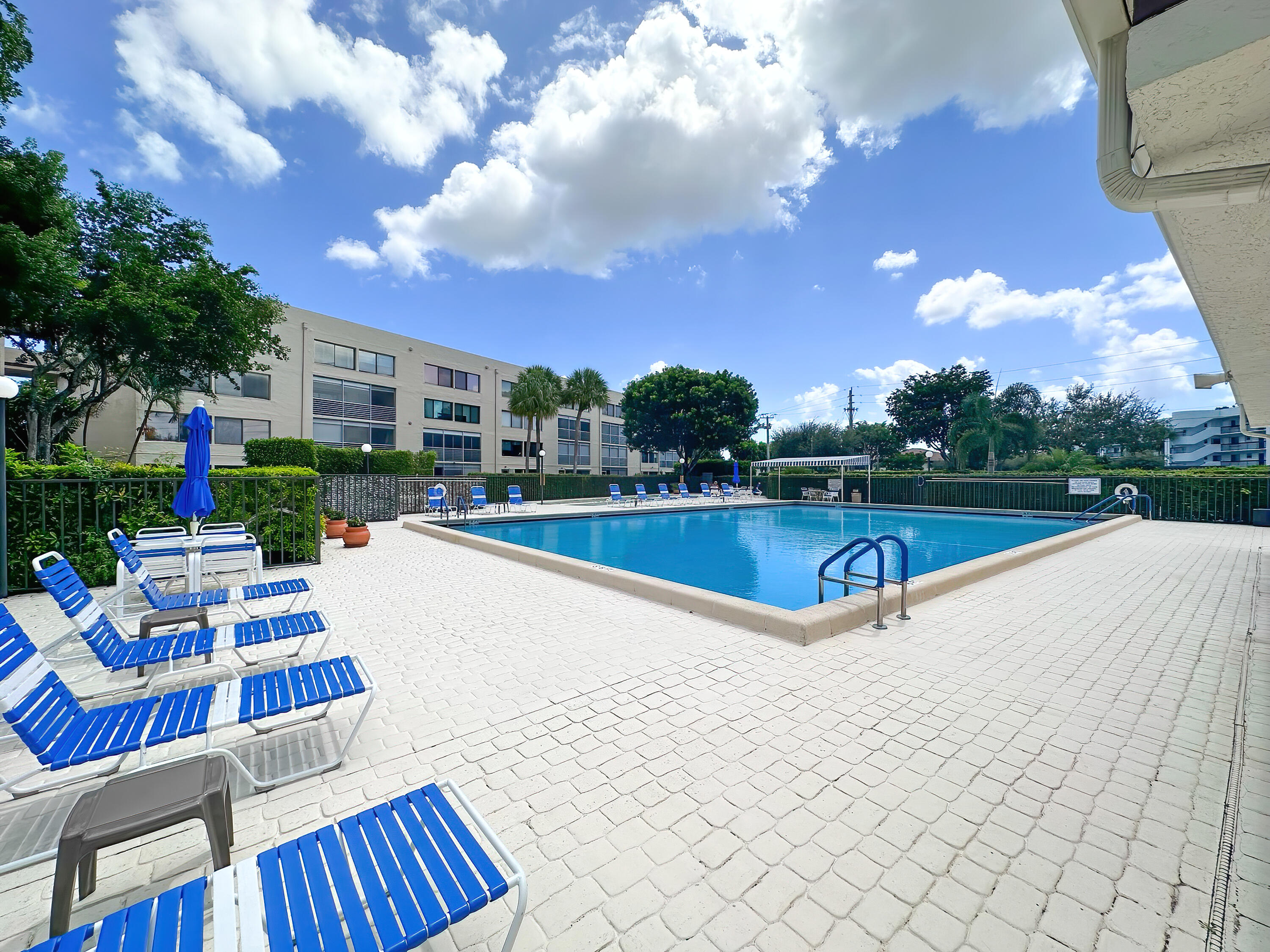 a view of swimming pool with seating space and trees in the background