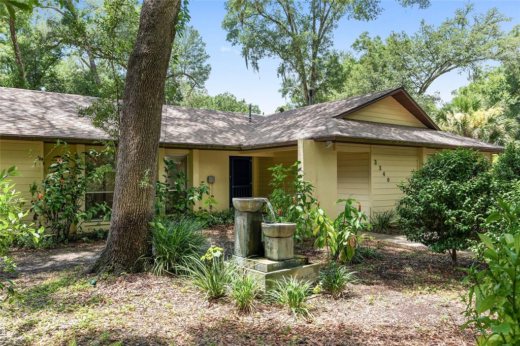 a view of a house with brick walls plants and large tree