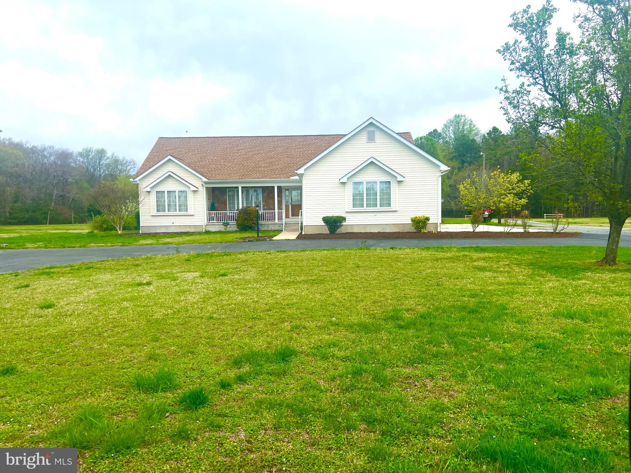 a house that is sitting in the grass with large trees and plants