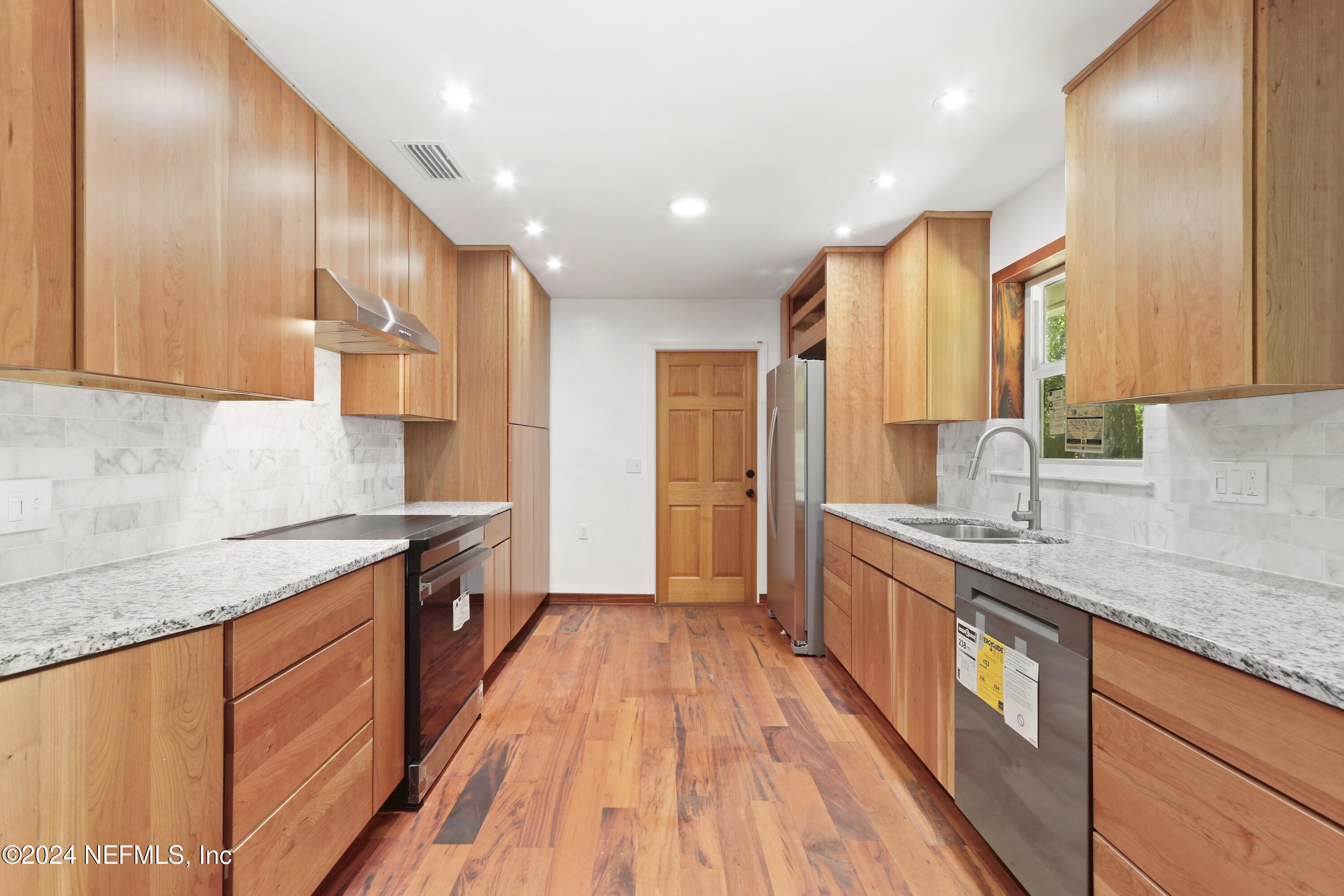 a large kitchen with stainless steel appliances granite countertop wooden floors a stove a sink and a white cabinets