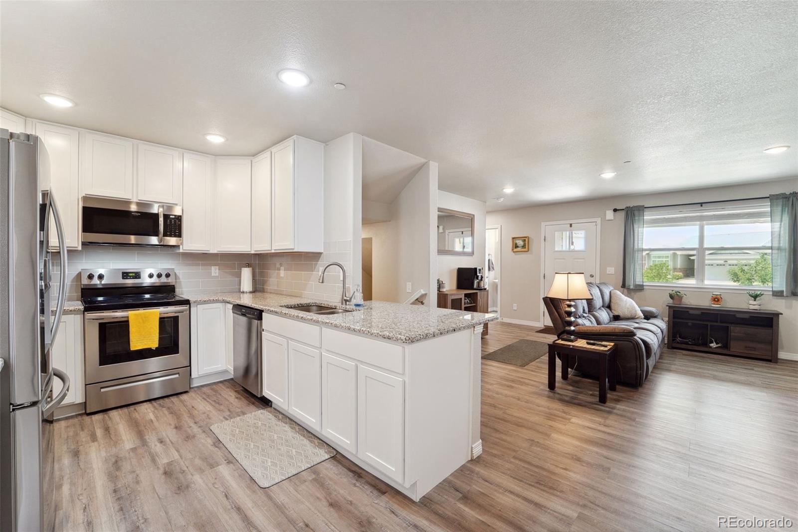 a living room with stainless steel appliances granite countertop furniture wooden floor and a view of kitchen