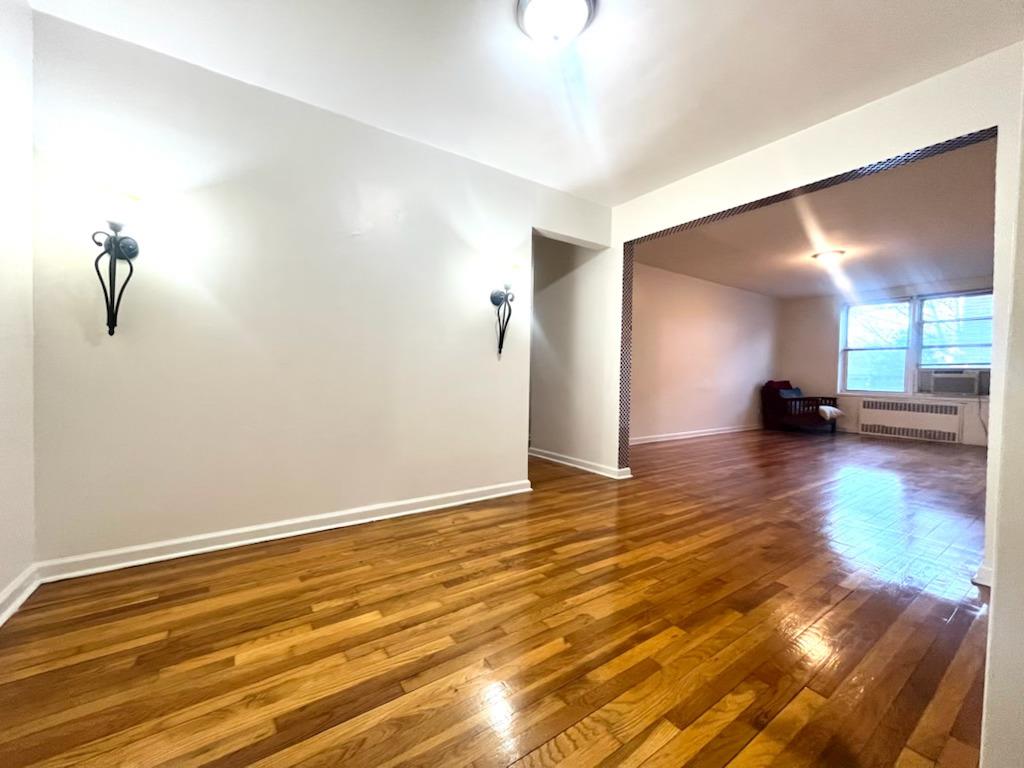 Additional living space featuring radiator heating unit, cooling unit, and wood-type flooring