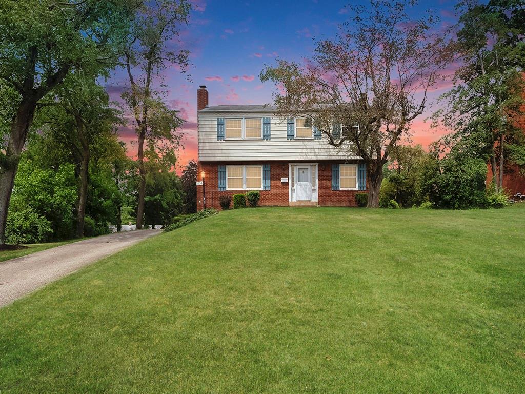 a view of a house next to a big yard and large trees