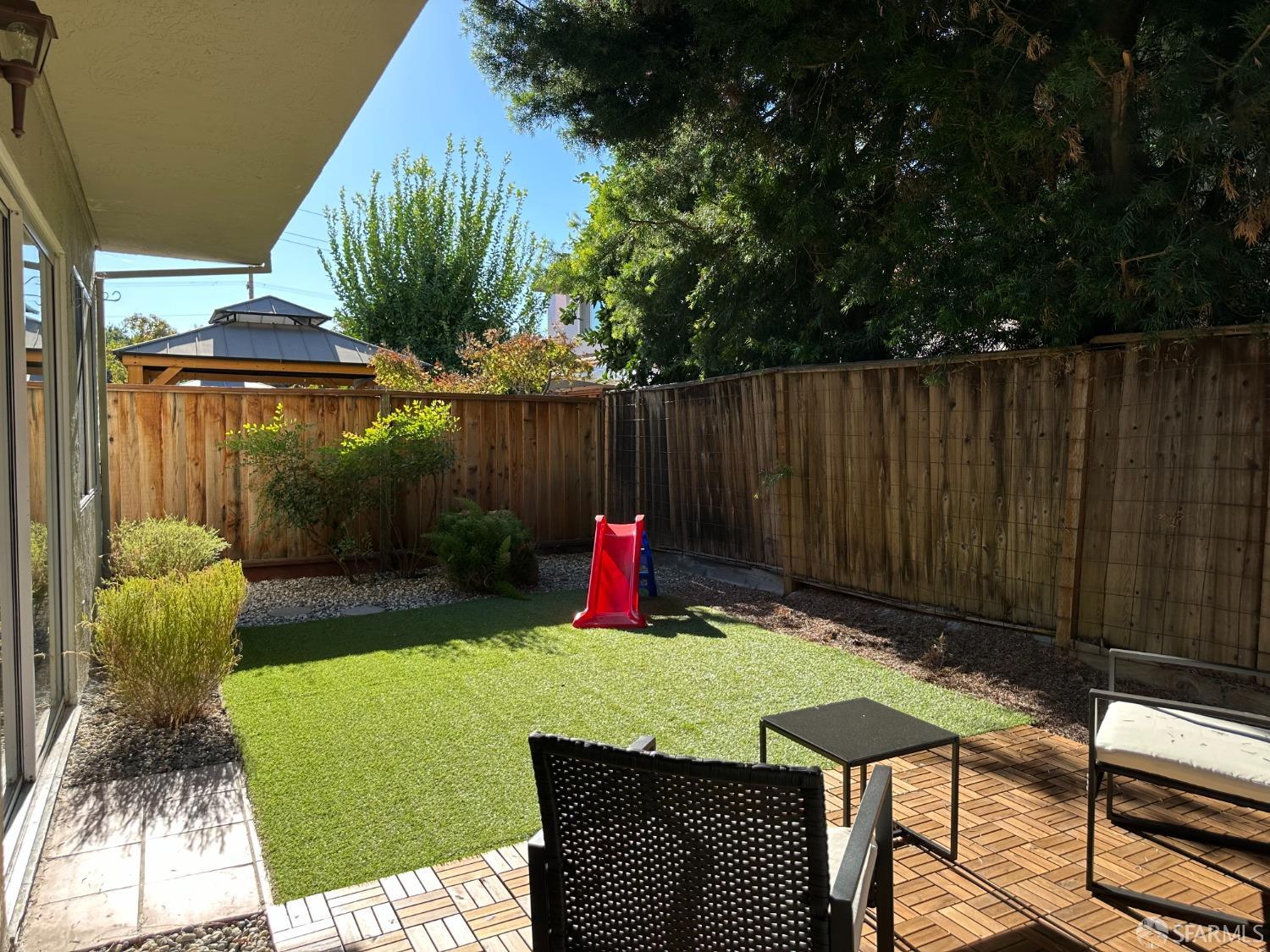 a view of a backyard with table and chairs potted plants and large tree