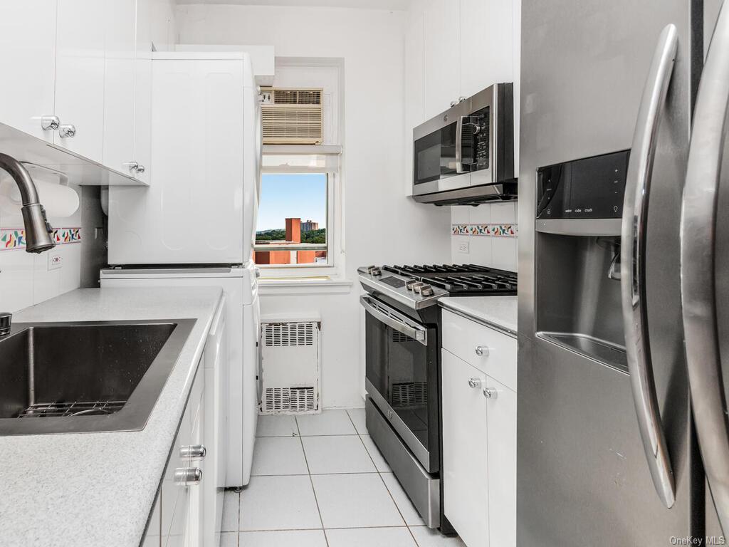 Kitchen with radiator heating unit, white cabinets, appliances with stainless steel finishes, and light tile patterned flooring