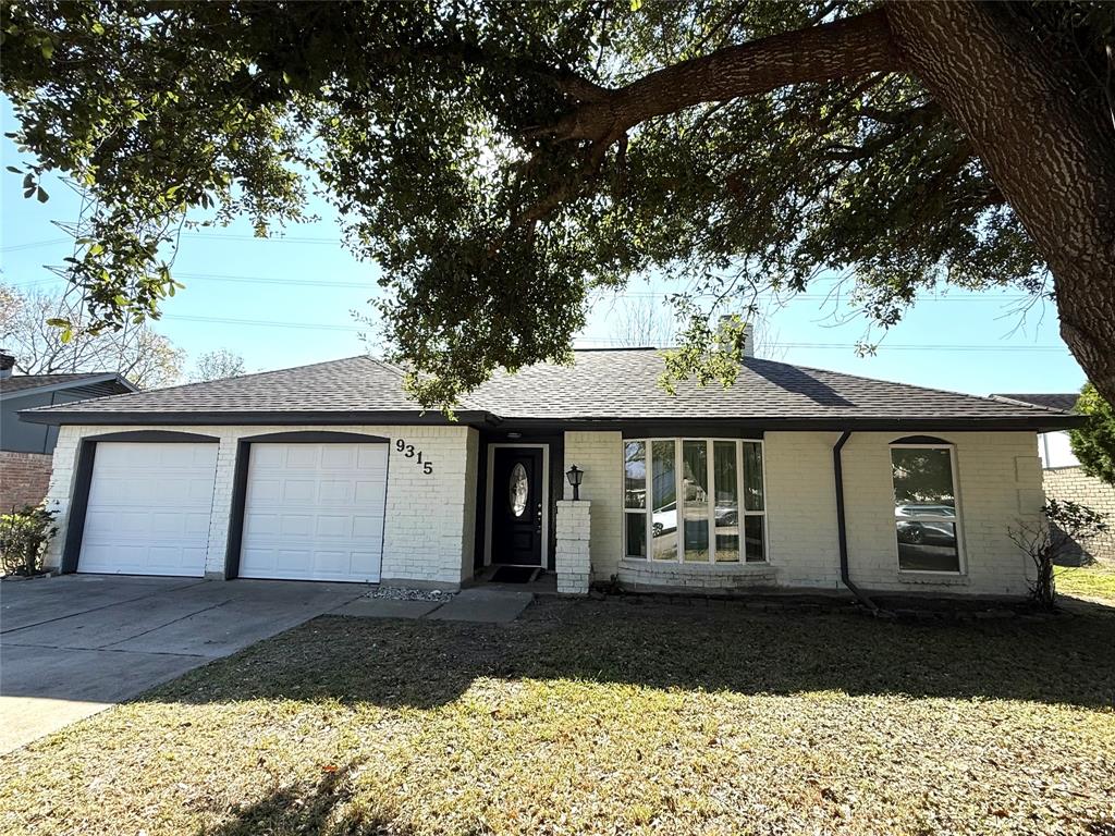 This charming single-story home features a brick exterior with a two-car garage. It has a well-maintained front yard and a large tree providing shade. The house has a welcoming entrance with a decorative front door and large windows for natural light.