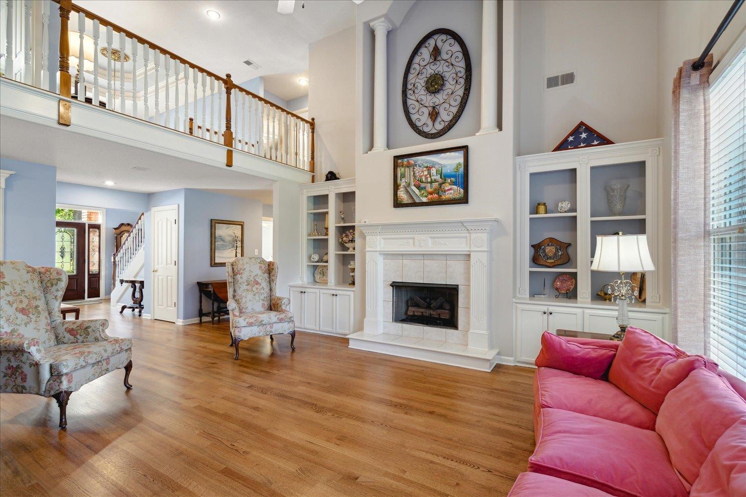 Living room with light hardwood / wood-style floors, ornate columns, a tiled fireplace, and a high ceiling