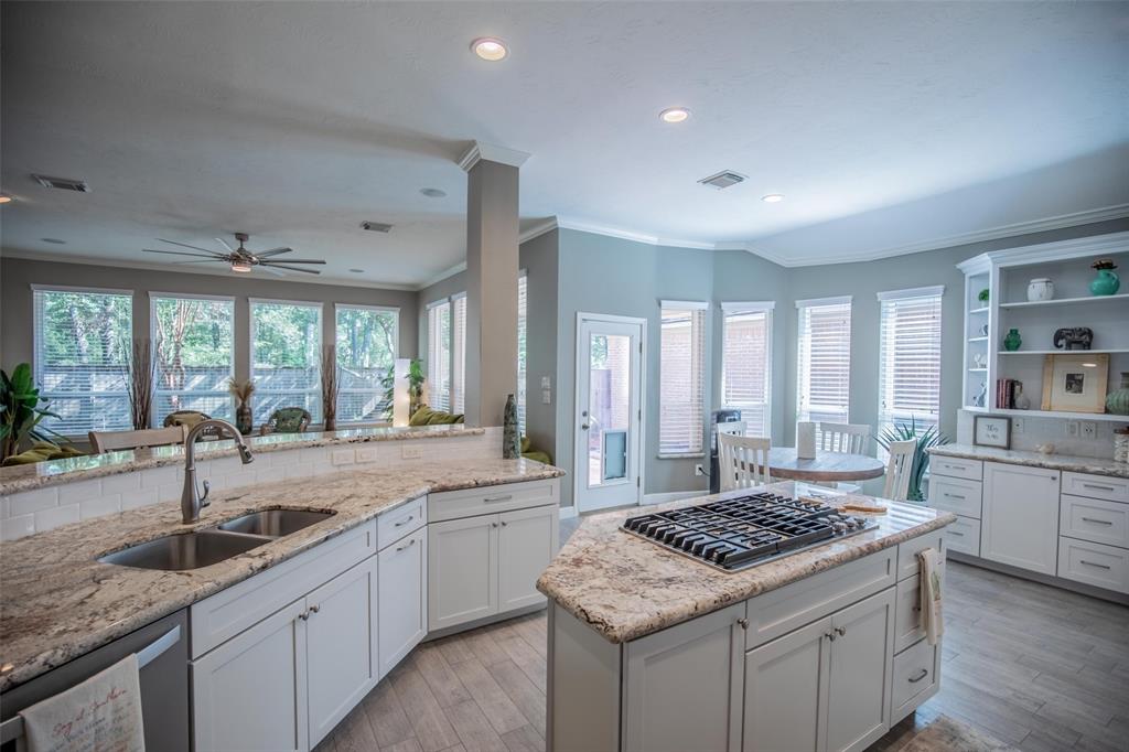 Open-concept kitchen with white cabinetry, stainless steel appliances, and granite countertops. It features a gas cooktop on the island and a built-in oven. The kitchen opens into a spacious living area.