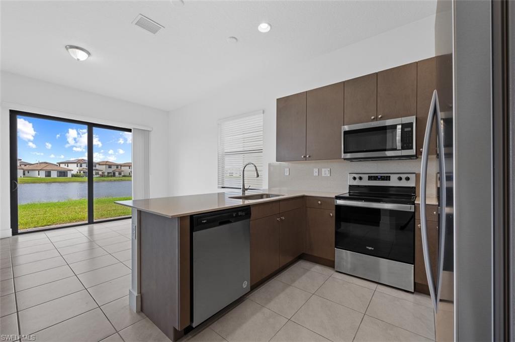 Kitchen featuring appliances with stainless steel finishes, a water view, light tile patterned flooring, kitchen peninsula, and sink