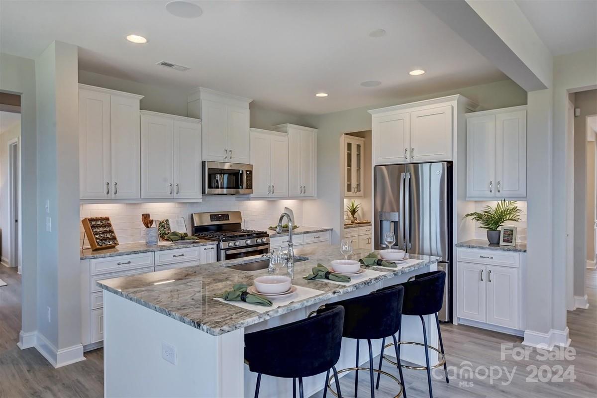 a kitchen with stainless steel appliances granite countertop a sink a stove a refrigerator a microwave a dining table and chairs with wooden floor