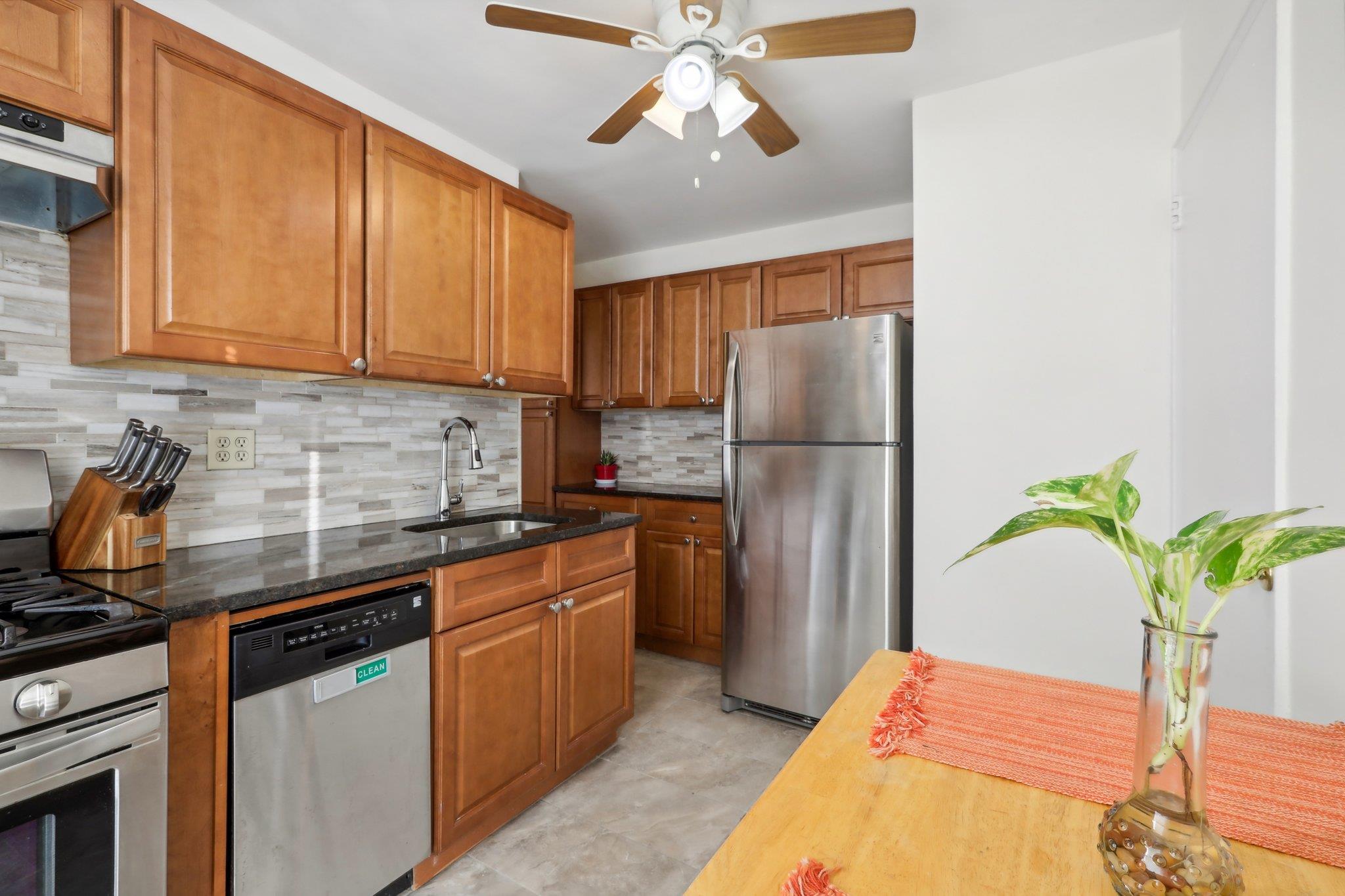 Kitchen featuring backsplash, stainless steel appliances, ceiling fan, sink, and dark stone countertops