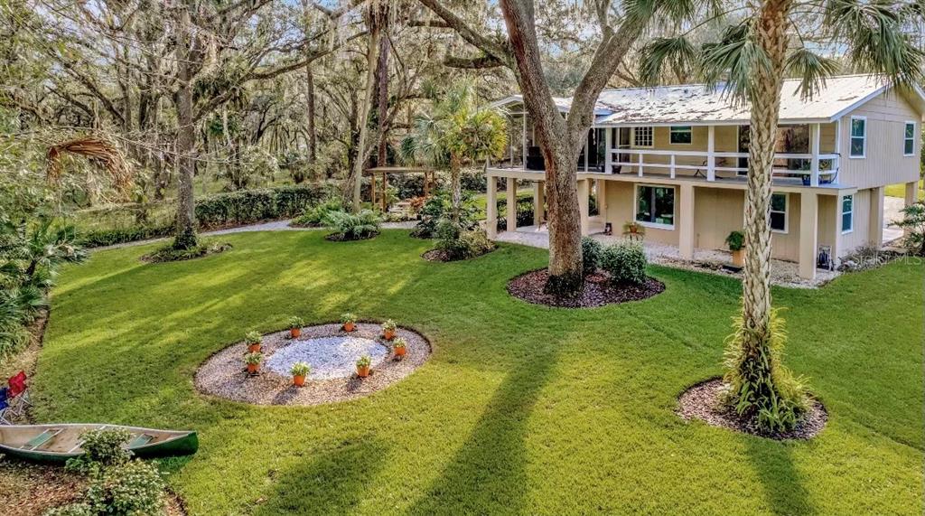 a view of a white house with a big yard and potted plants and large trees