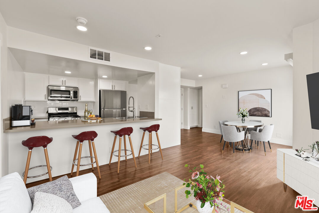 a living room with stainless steel appliances kitchen island granite countertop a table chairs and a refrigerator