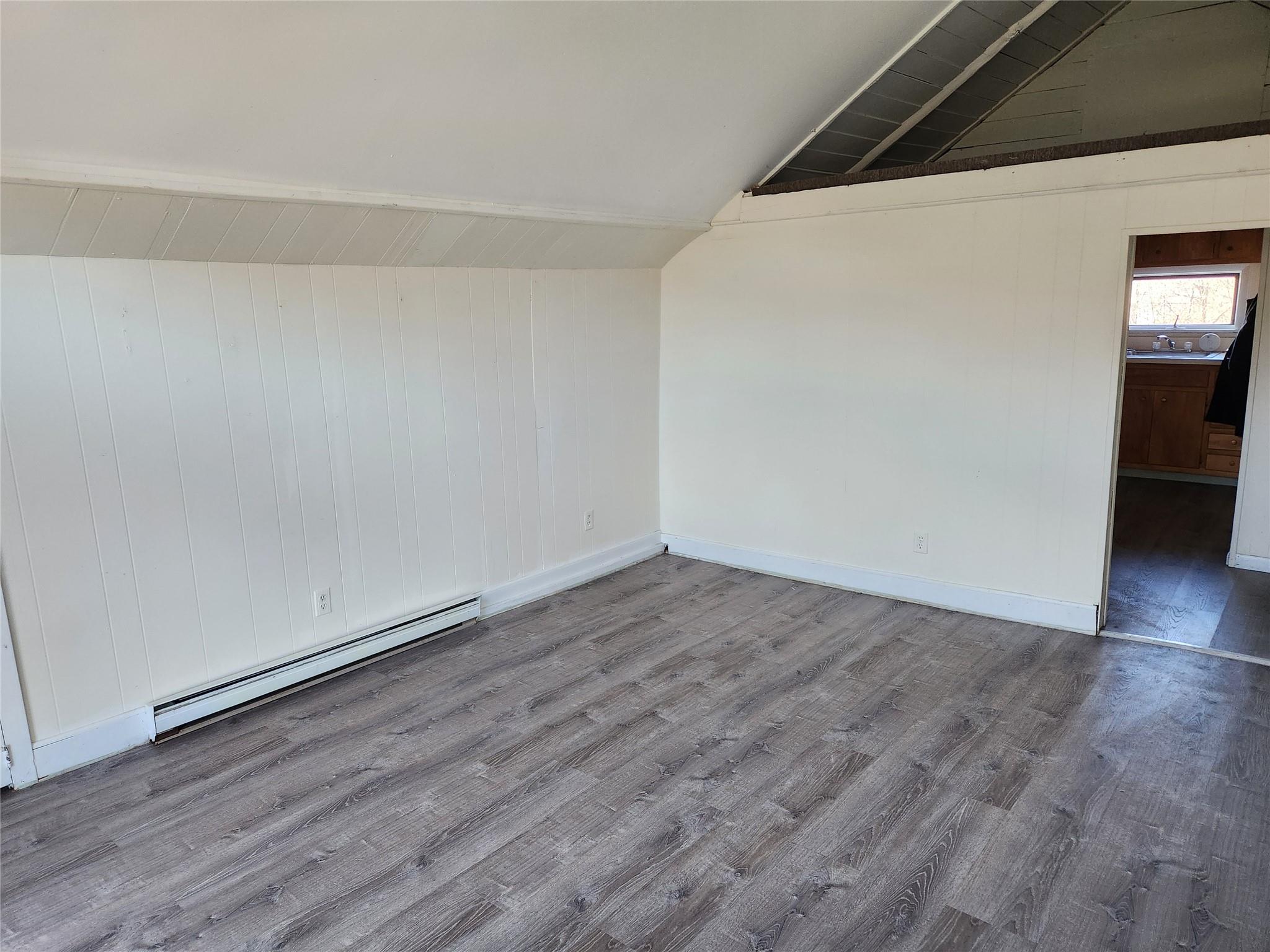 Spare room featuring hardwood / wood-style floors, a baseboard radiator, and vaulted ceiling