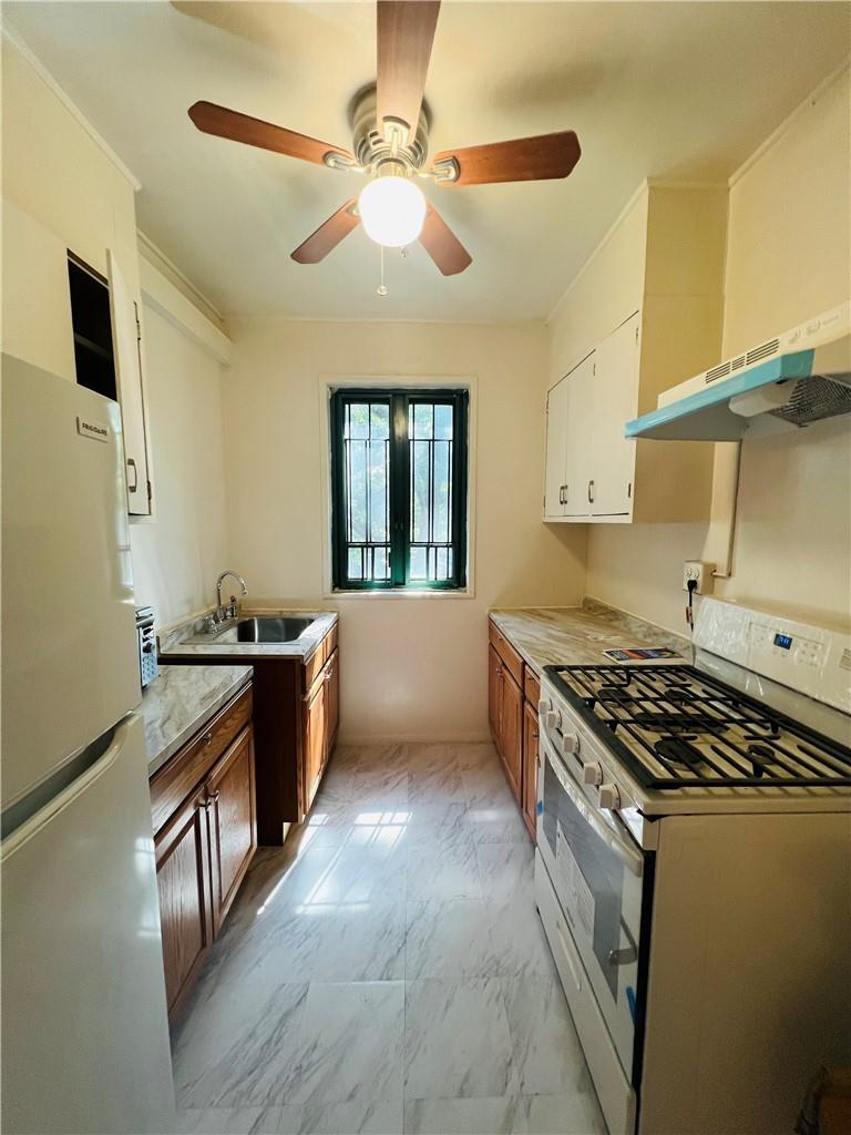 Kitchen with white range with gas stovetop, wall chimney exhaust hood, sink, fridge, and ceiling fan