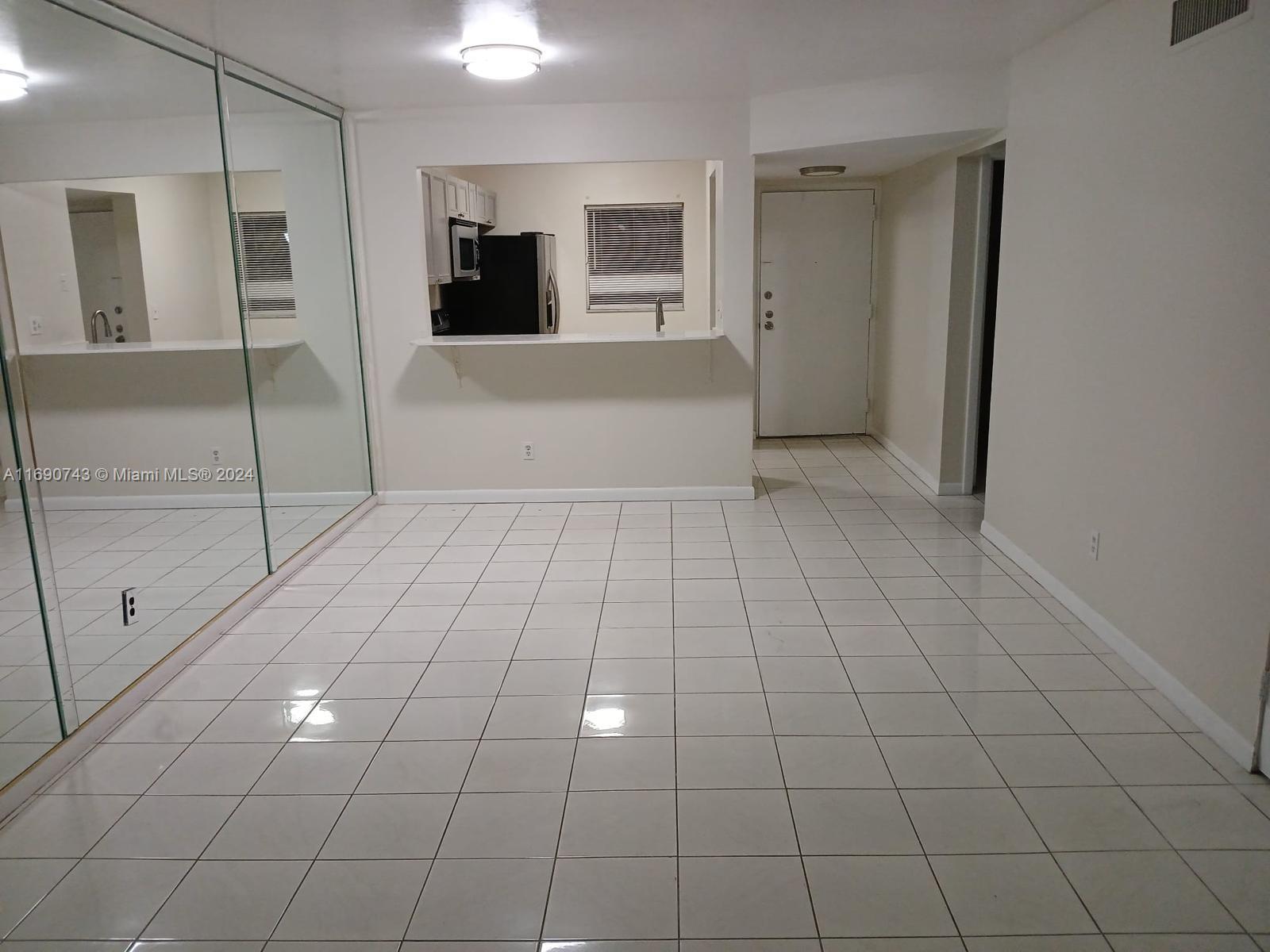 a view of a livingroom with an empty space & kitchen window