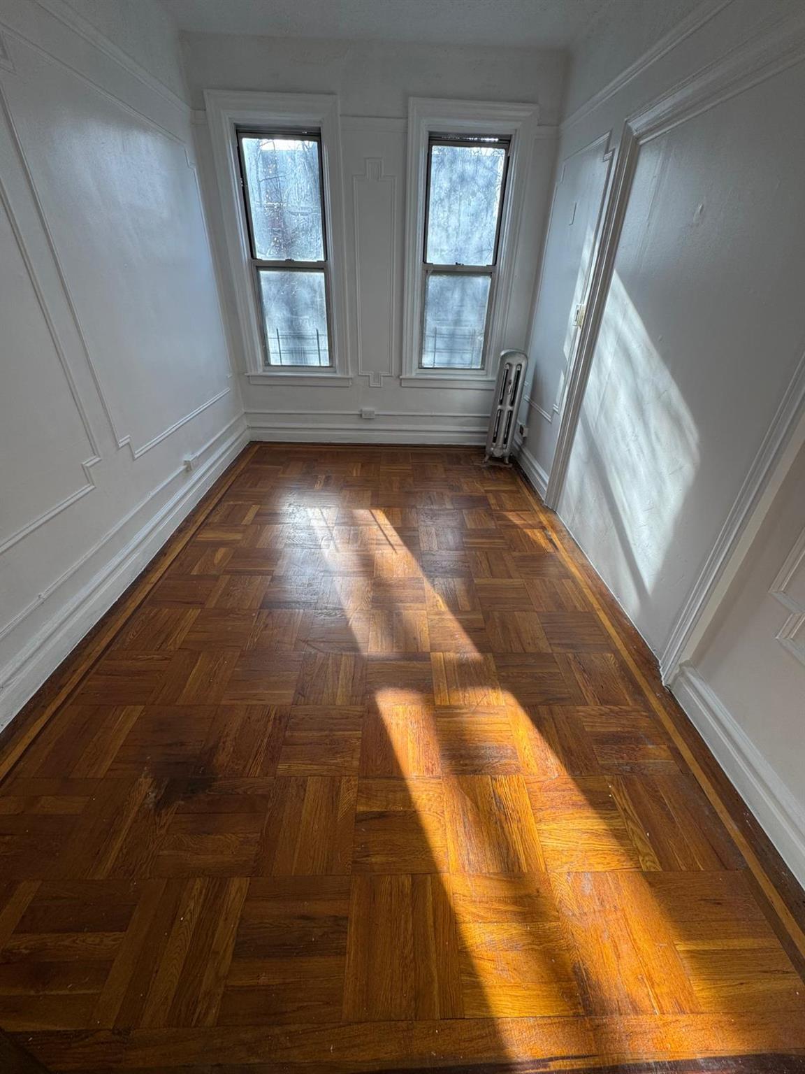 Empty room featuring dark parquet flooring and radiator