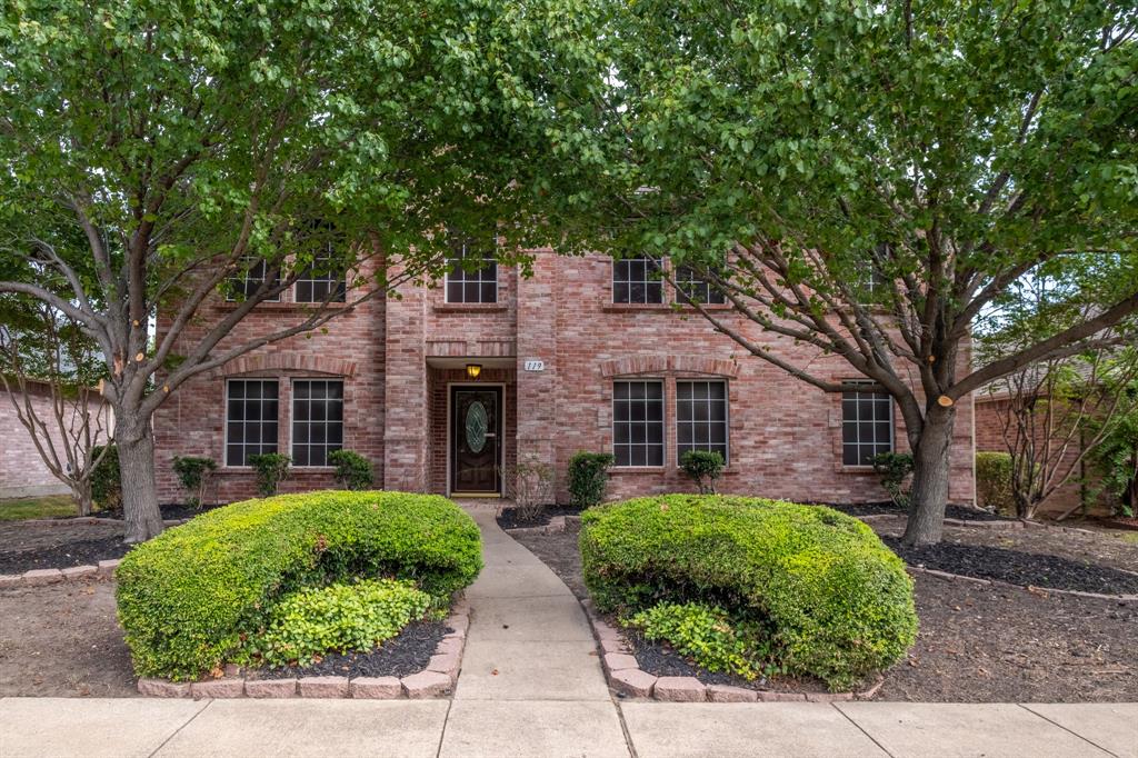 a brick house with a big yard plants and large trees