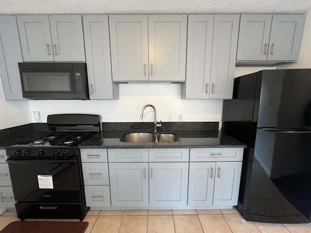 Kitchen with sink, dark stone countertops, a textured ceiling, light tile patterned flooring, and black appliances