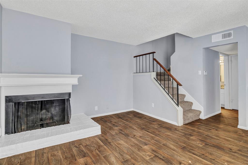 a view of an empty room with wooden floor fireplace and a window