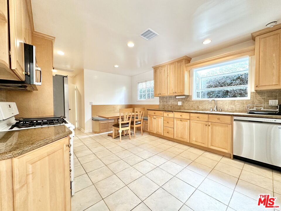 a kitchen with stainless steel appliances granite countertop a stove top oven a sink a dining table and chairs