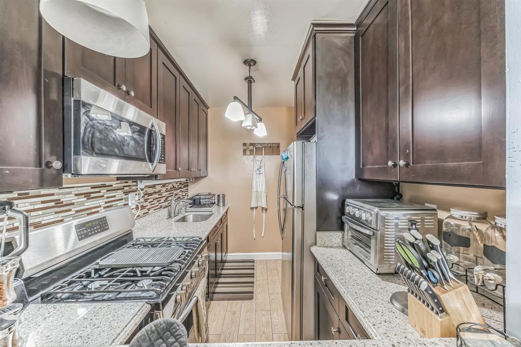 Kitchen featuring sink, hanging light fixtures, light stone countertops, light hardwood / wood-style floors, and stainless steel appliances