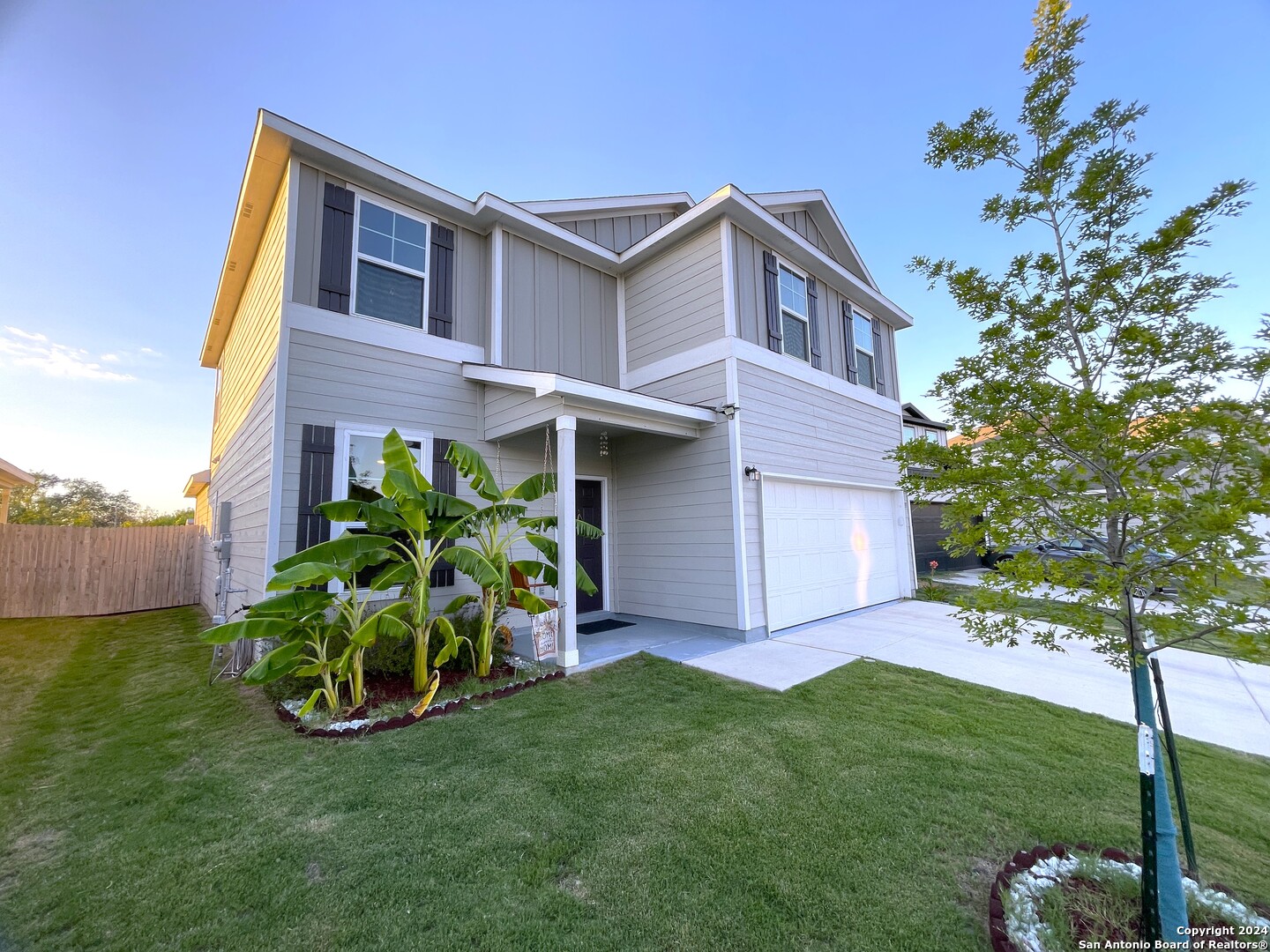 a house that has a big yard with potted plants and a large tree