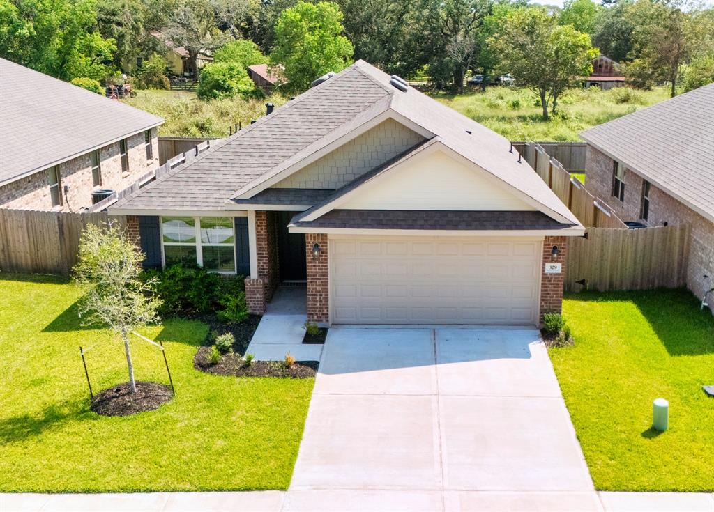 Aerial view of a single-story suburban home featuring a well-maintained lawn, an attached two-car garage, and a tidy landscape with trees.