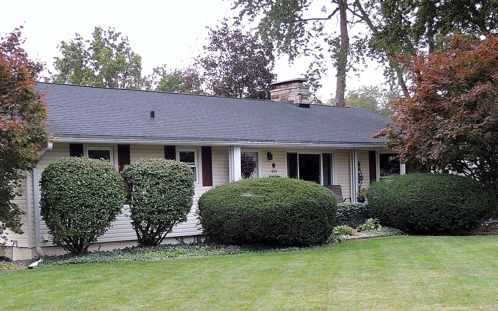 a view of a brick house with plants and large trees