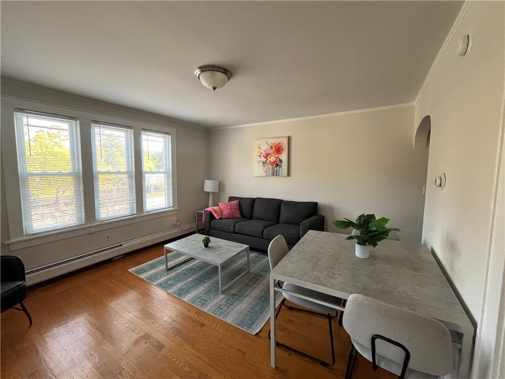 Living room with hardwood / wood-style floors, a baseboard heating unit, and crown molding