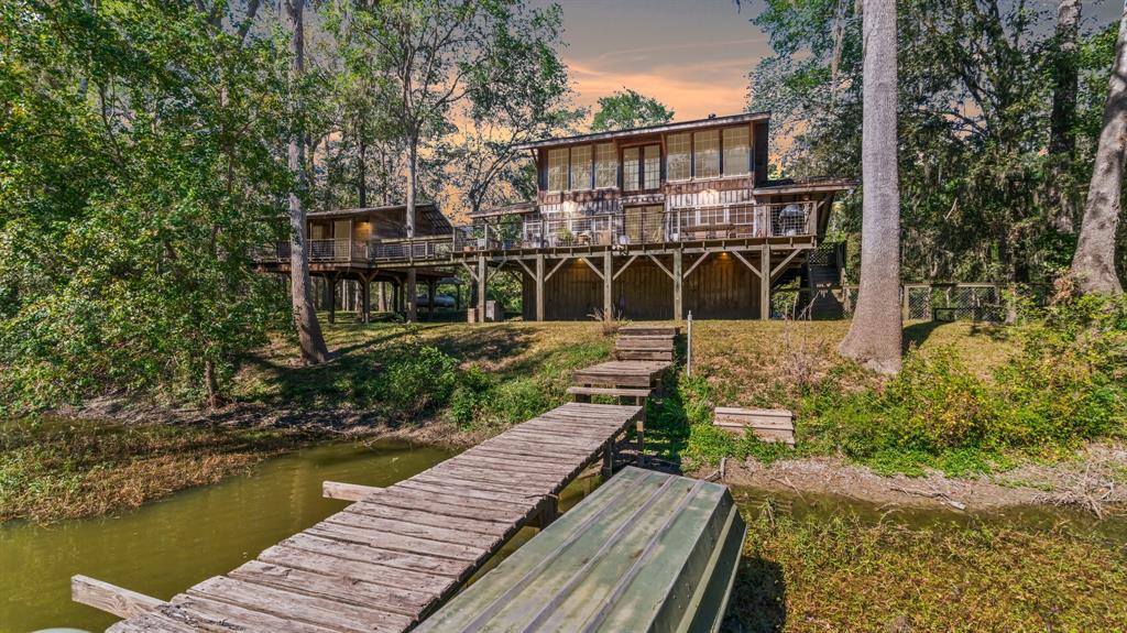 This is an elevated wooden home surrounded by natural scenery, featuring a spacious deck, a private pier leading to a tranquil waterway, and a fenced backyard.