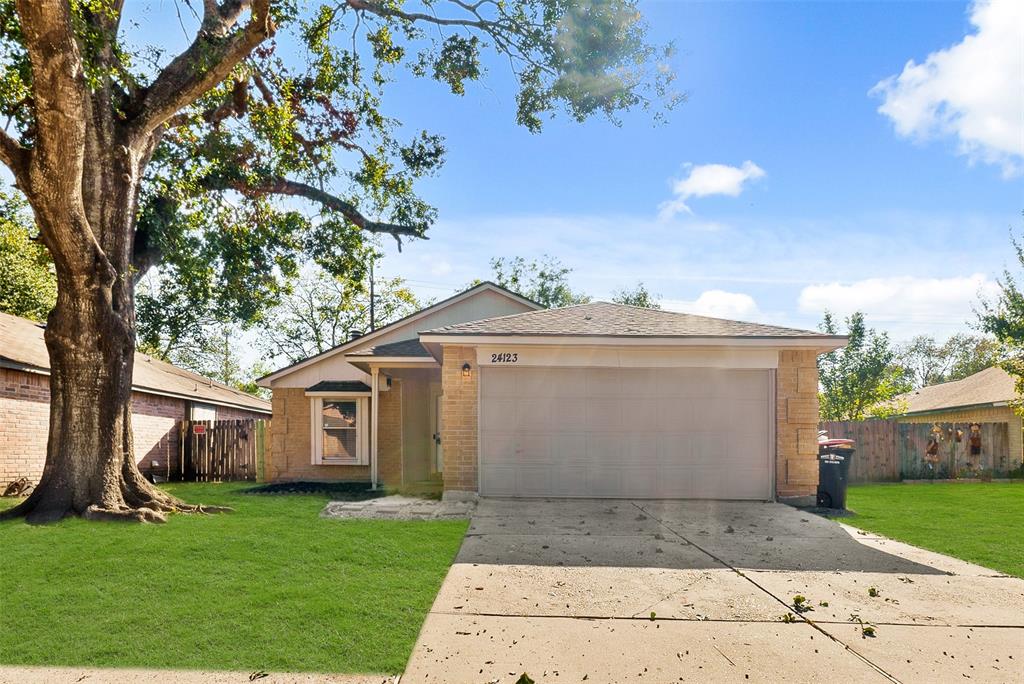 This is a single-story home featuring a two-car garage, a well-maintained front lawn with a mature tree, and a cozy entrance.