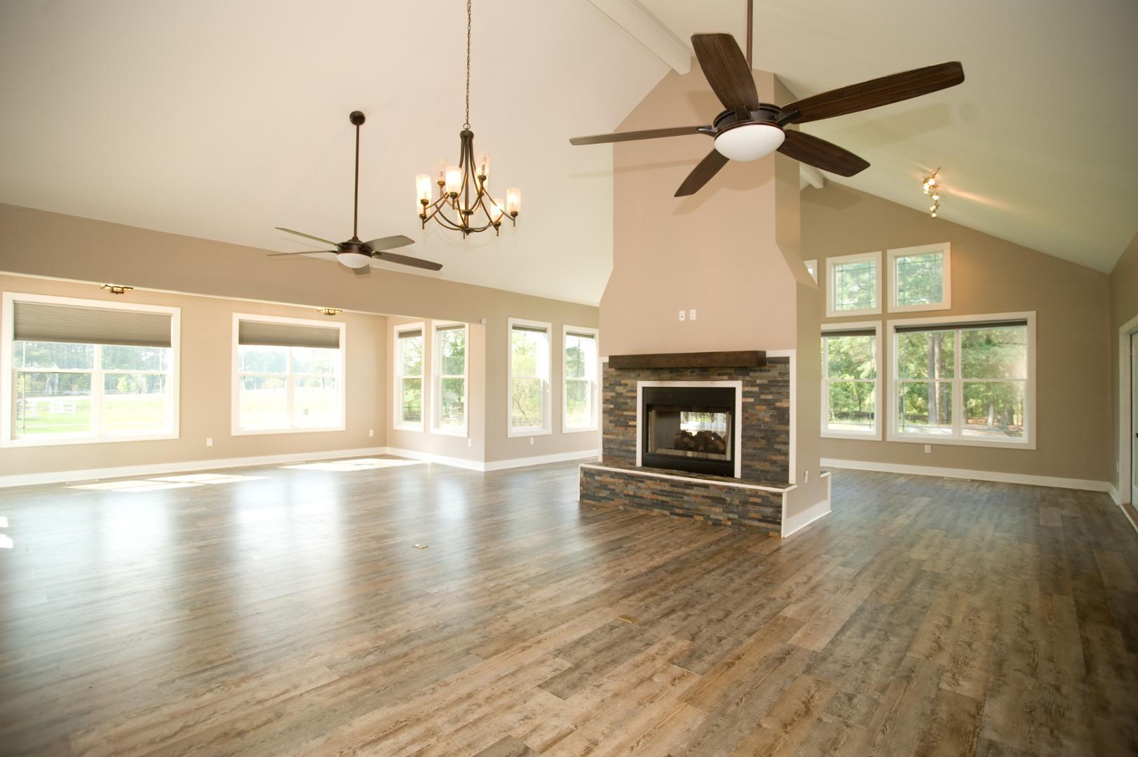 an empty room with wooden floor a fireplace a ceiling fan and windows